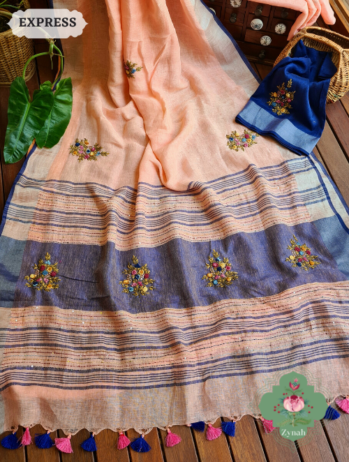 Peach colored, pure linen saree with a shimmering zari border. The saree features intricate french-knot embroidered butis and traditional kantha work on the pallu.