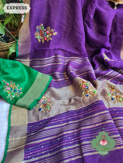 Aubergine colored pure linen saree with a gleaming zari border and detailed french-knot embroidered butis. The pallu showcases intricate kantha work designs adding an ethnic touch.