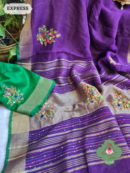Aubergine colored pure linen saree with a gleaming zari border and detailed french-knot embroidered butis. The pallu showcases intricate kantha work designs adding an ethnic touch.