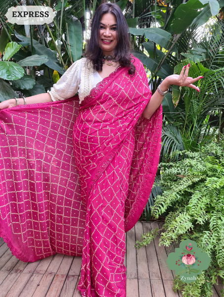 A hot pink crepe silk saree with bandhani inspired prints and detailed mirror work on the scalloped borders.
