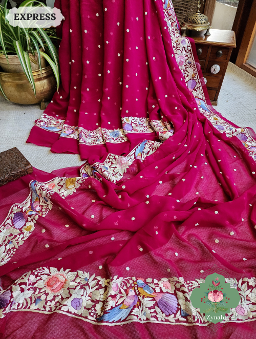 A vibrant Fuschia Pink saree made of Crepe Silk with Hand-Embroidered Parsi Gara work. The saree features intricate floral motifs.