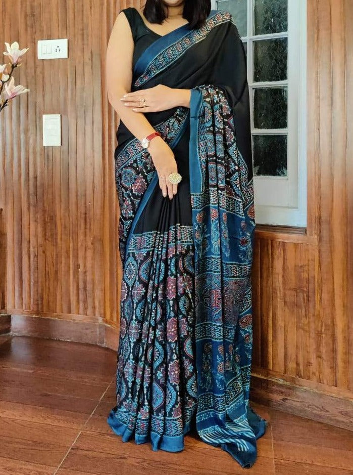A woman showcasing a black and blue pure modal silk saree with handblock prints, along with an attached blouse piece.